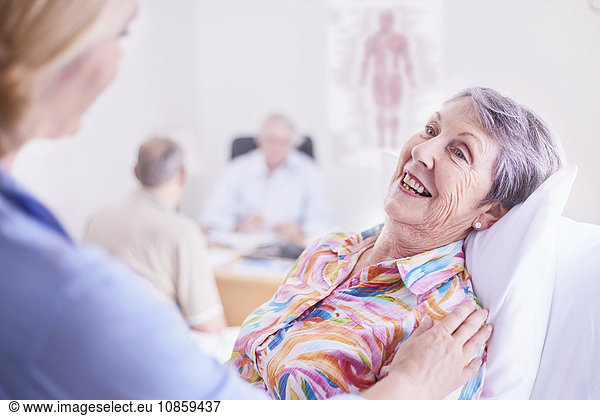 Ärztin tröstet lächelnde Seniorin bei der Untersuchung