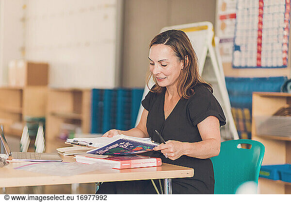1st Grade Teacher holding books and clipboard in classroom