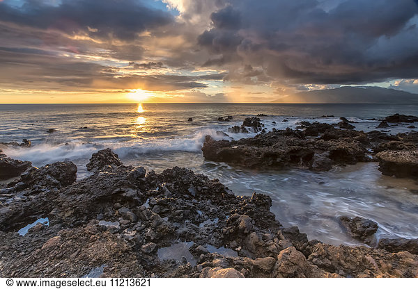 'Sunset over the ocean and water washing over rocks on the shore; Maui  Hawaii  United States of America'