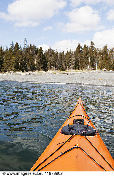 'The orange tip of a kayak in water facing the shore and forest in Kachemak Bay; Alaska  United States of America '