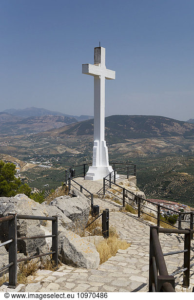 'Walkway with railing to a large  white stone cross with mountains in the distance; Jaen  Spain'