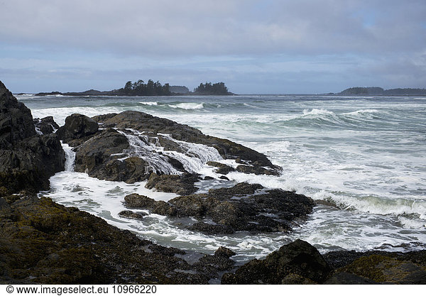'Waves washing over rocks and waves along the coastline under a cloudy sky; Tofino British Columbia Canada'