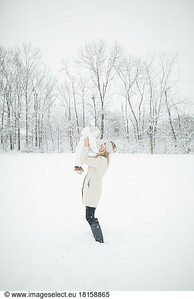 30-year-old blonde Caucasian mother holds up baby in snow.