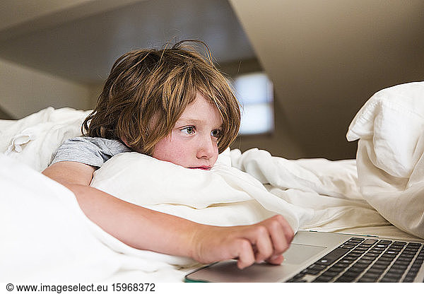 6 year old boy looking at laptop compuetr in his bedroom
