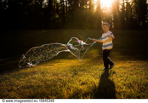 5 year old boy making giant bubble at golden hour