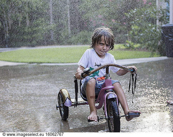 5 year old boy riding his tricycle bike in the rain