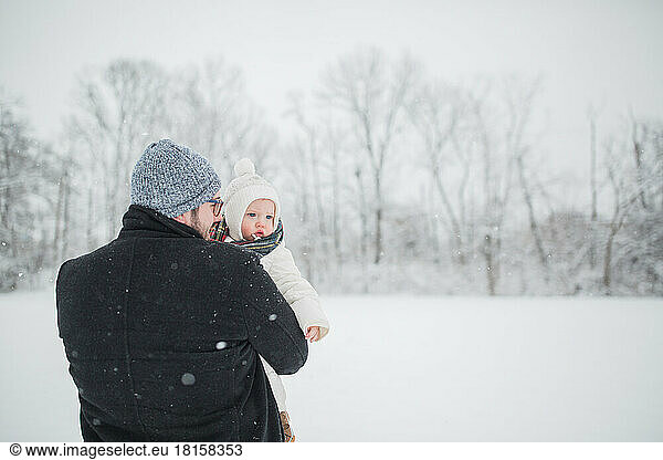 30-year-old Caucasian father holds baby boy in snowy field.