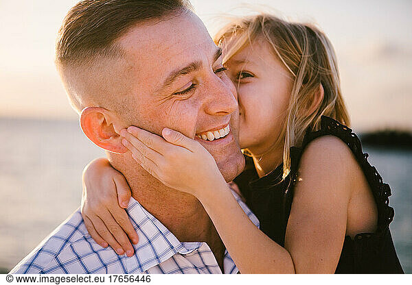 5 year old daughter gives father a kiss on the cheek by ocean
