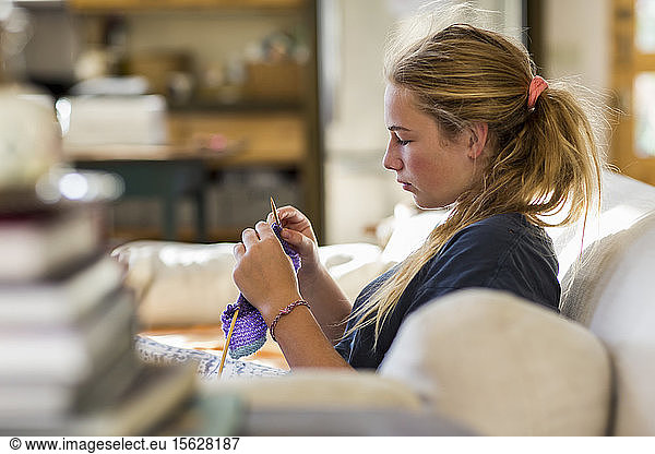 13 year old girl knitting on couch in early morning light