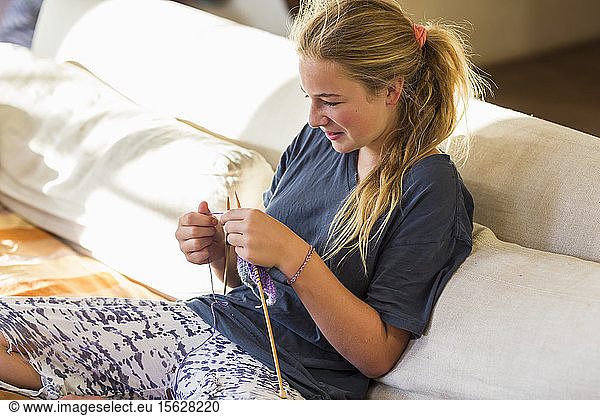13 year old girl knitting on couch in early morning light