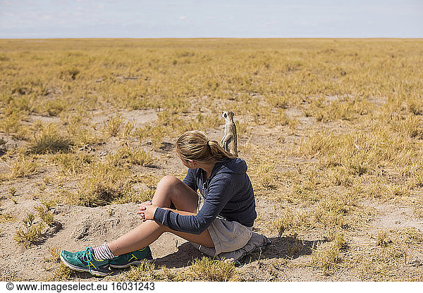 12 year old girl sitting watching meerkats emerge from their burrows  in the Kalahari desert.