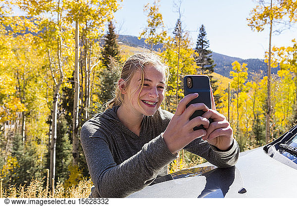 13 year old girl taking pictures with her smart phone  looking at autumn aspen trees