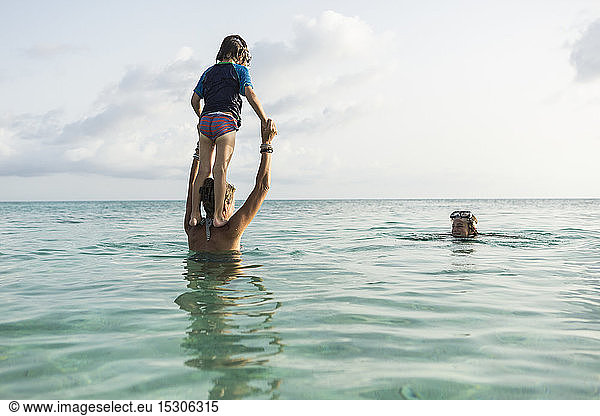 5 year old son on mother's shoulders leaping into the ocean at sunset