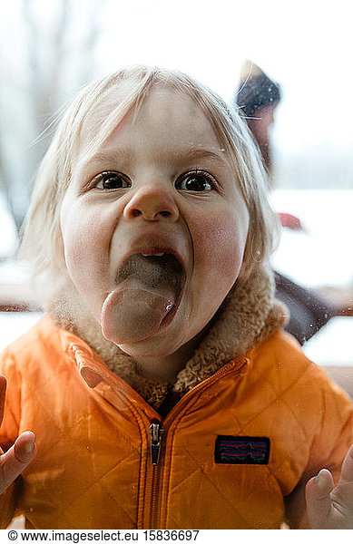 3 year old toddler girl smashes her tongue and face against window