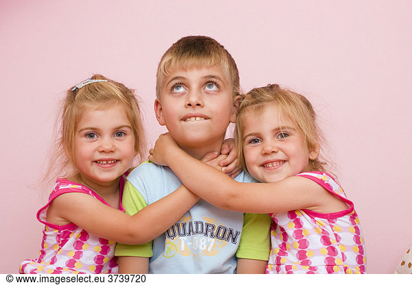 3 year old twin girls embracing a seven year old boy