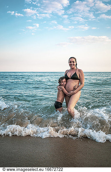 5 years old kid hugging pregnant mother  knee deep in the ocean