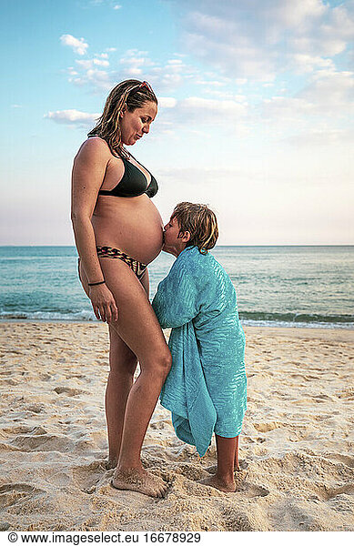 5 years old kid kissing the belly of his pregnant mother  at the beach