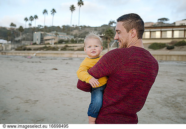 30 yr old dad at the beach holding 6 mo old blond baby