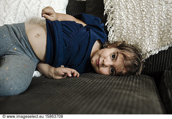 4 yr old girl lying on couch with belly showing