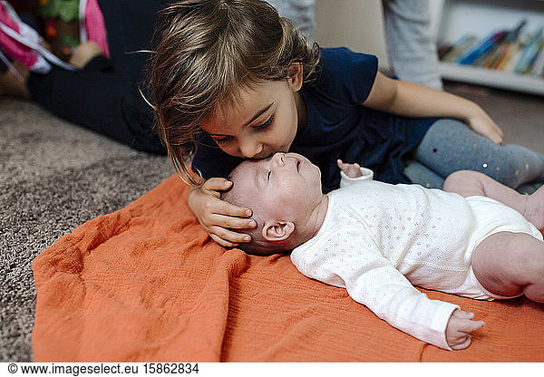 4 yr old kissing infant sister on orange blanket on floor