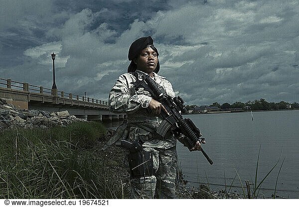 A African American  female  Air Force Security Forces Airman in uniform poses with her M-4 rifle near the shoreline of a river.