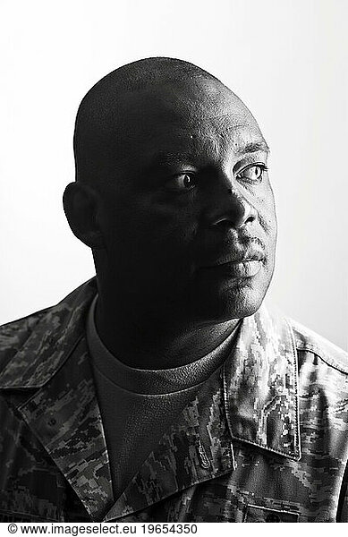 A African American  male  Air Force Security Forces Airman in uniform sits for a profile black and white portrait with a white backdrop.