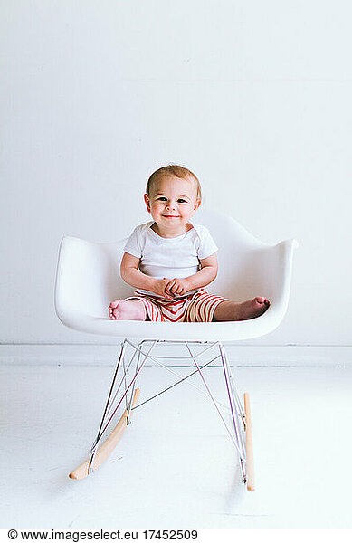 A baby boy sits in a modern shell chair