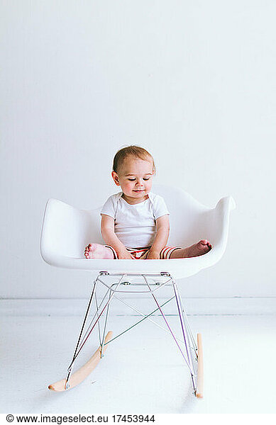 A baby boy sits in a modern shell chair