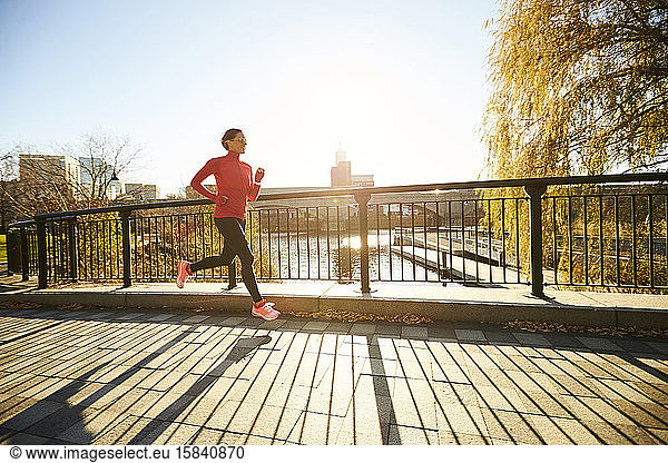 A backlit woman running over a footbridge in a city park.