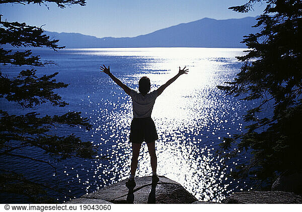 A backlit woman with her arms outstretched  standing on a rock overlooking Lake Tahoe  California.