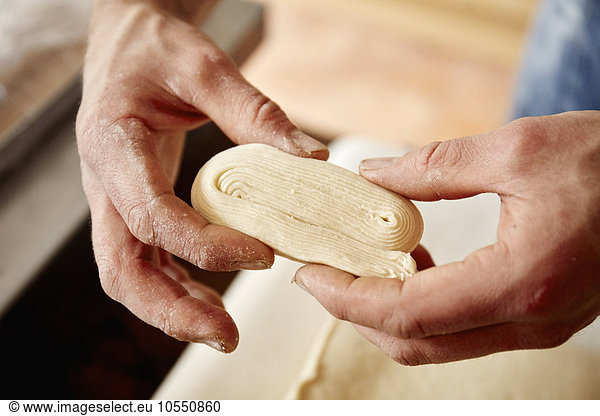 A baker holding dough which has been folded and worked to show the layers incorporated into the dough  to make light layered pastries.