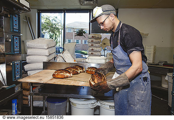 A baker wearing oven mitts carries a loaf of fresh-baked bread