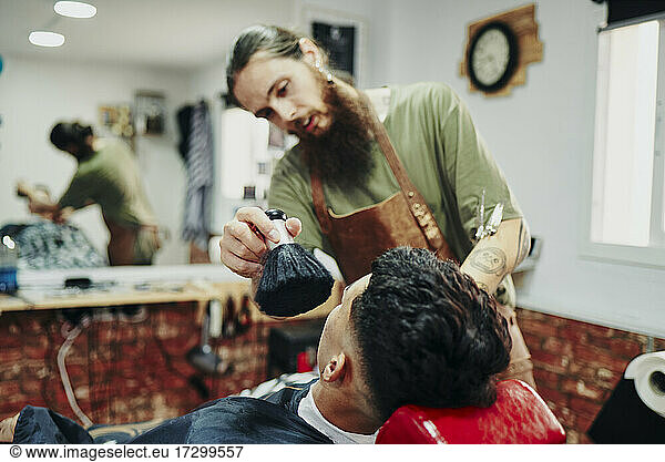 A barber cleaning the face of hair with a feather duster.