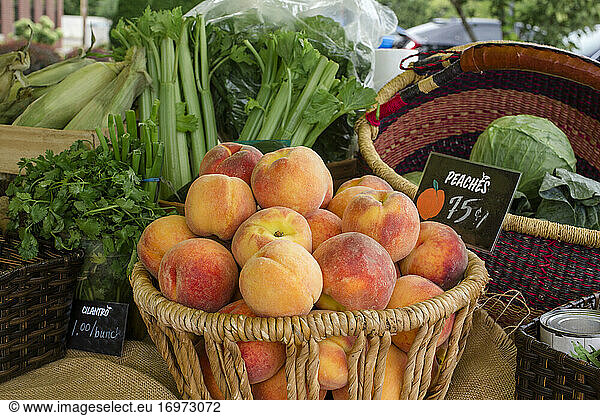 A basket of fresh peaches sits on table of small farm stand outdoors
