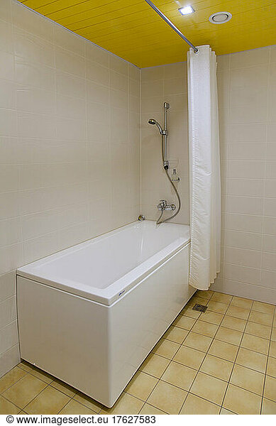 A bathroom  bathtub and wall mounted shower and shower curtain  tiled floor and yellow ceiling.
