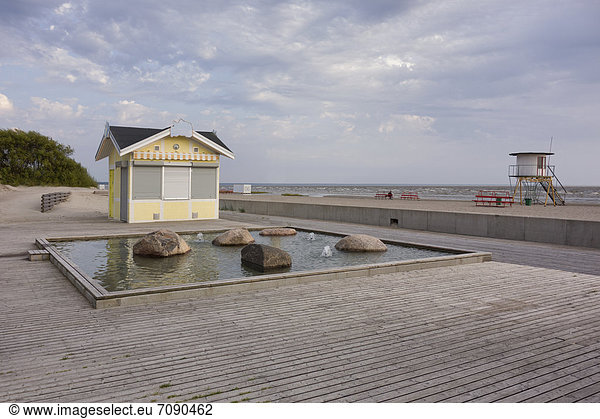 A beach resort on the Baltic sea coast. A kiosk with the shutters down  and a viewing tower on the sand. Offseason.