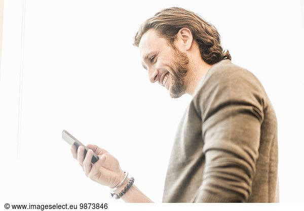 A bearded man smiling and checking his phone.