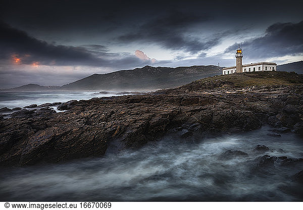A beautiful lighthouse on a hill with its light on at sunset