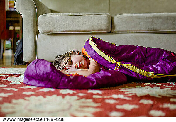 A beautiful little girl rests in a sleeping bag on the floor indoors