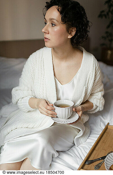 A beautiful woman has breakfast in a white bed at home