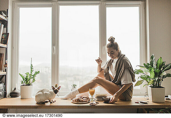 a beautiful woman with a cat sitting at the window having breakfast