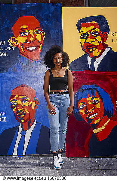 A beautiful young artist stands proudly in front of her street mural