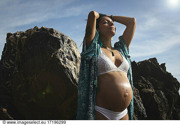 A beautiful young woman pregnant at beach with stones in a warm summer