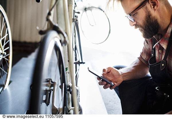 A bike mechanic in a bicycle repair shop using a smart phone.
