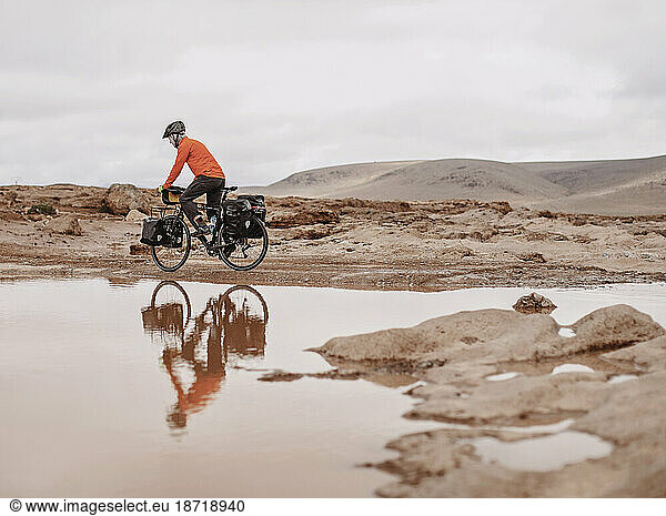 A bike packer is reflected in water on a cold day  Taliouine  Morocco