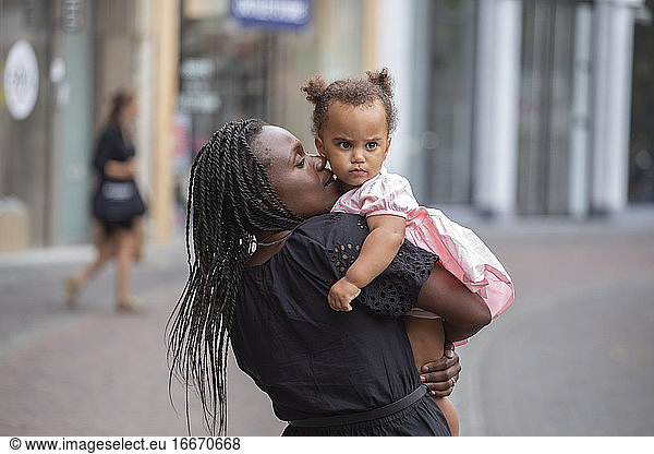 A black mother cuddles her daughter in the city
