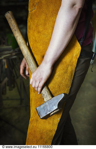A blacksmith in a heatproof apron holding a large hammer.