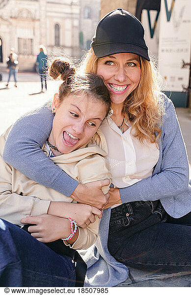 A blond woman and a teen daughter are sitting and hugging
