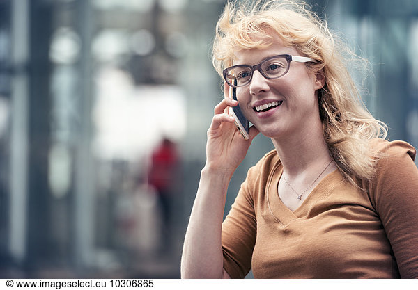 A blond woman talking on a cell phone on a street in the city
