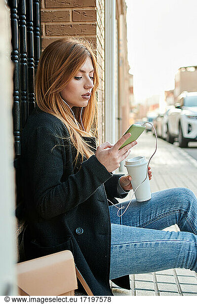 A blonde business woman is drinking coffee and looking at her phone